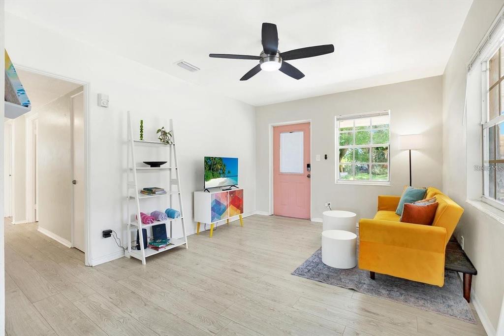 A living room features light wood-look flooring, a yellow sofa, and a pink front door — 6490 34TH AVENUE N, ST PETERSBURG, FL