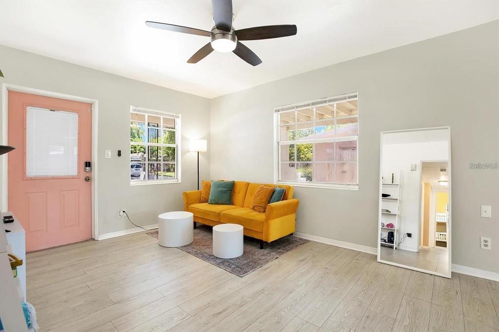 A living room features a yellow sofa, a pink door, and light wood-look flooring — 6490 34TH AVENUE N, ST PETERSBURG, FL
