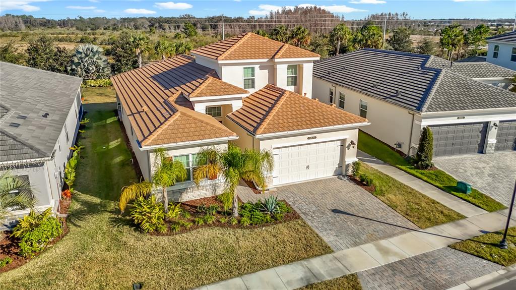 An aerial view shows a tan stucco house with a tiled roof and paver driveway — 32676 TREE OF LIFE AVENUE, WESLEY CHAPEL, FL