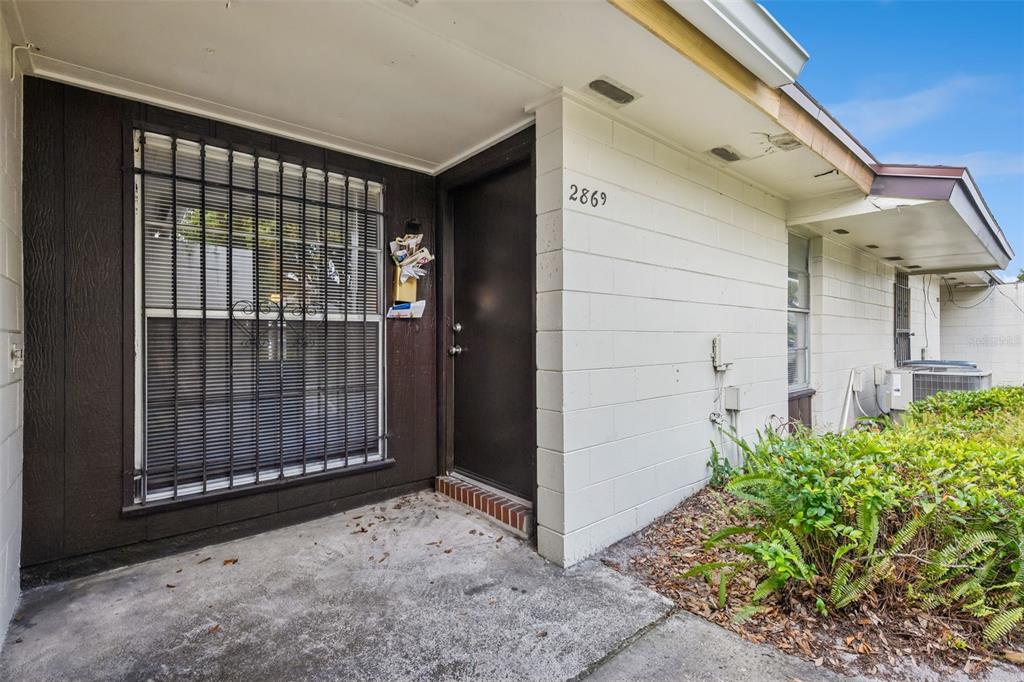A concrete block house exterior features a front door, a barred window, and a small porch — 2869 WILLOW RUN, ORLANDO, FL