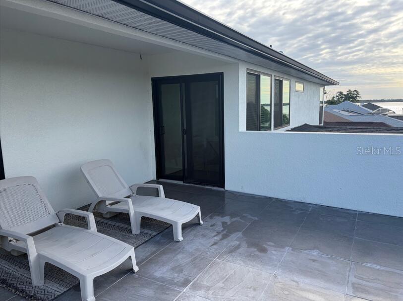 A tiled balcony features two lounge chairs and a sliding glass door overlooking the water — 14150 OSTROM AVENUE, PORT CHARLOTTE, FL