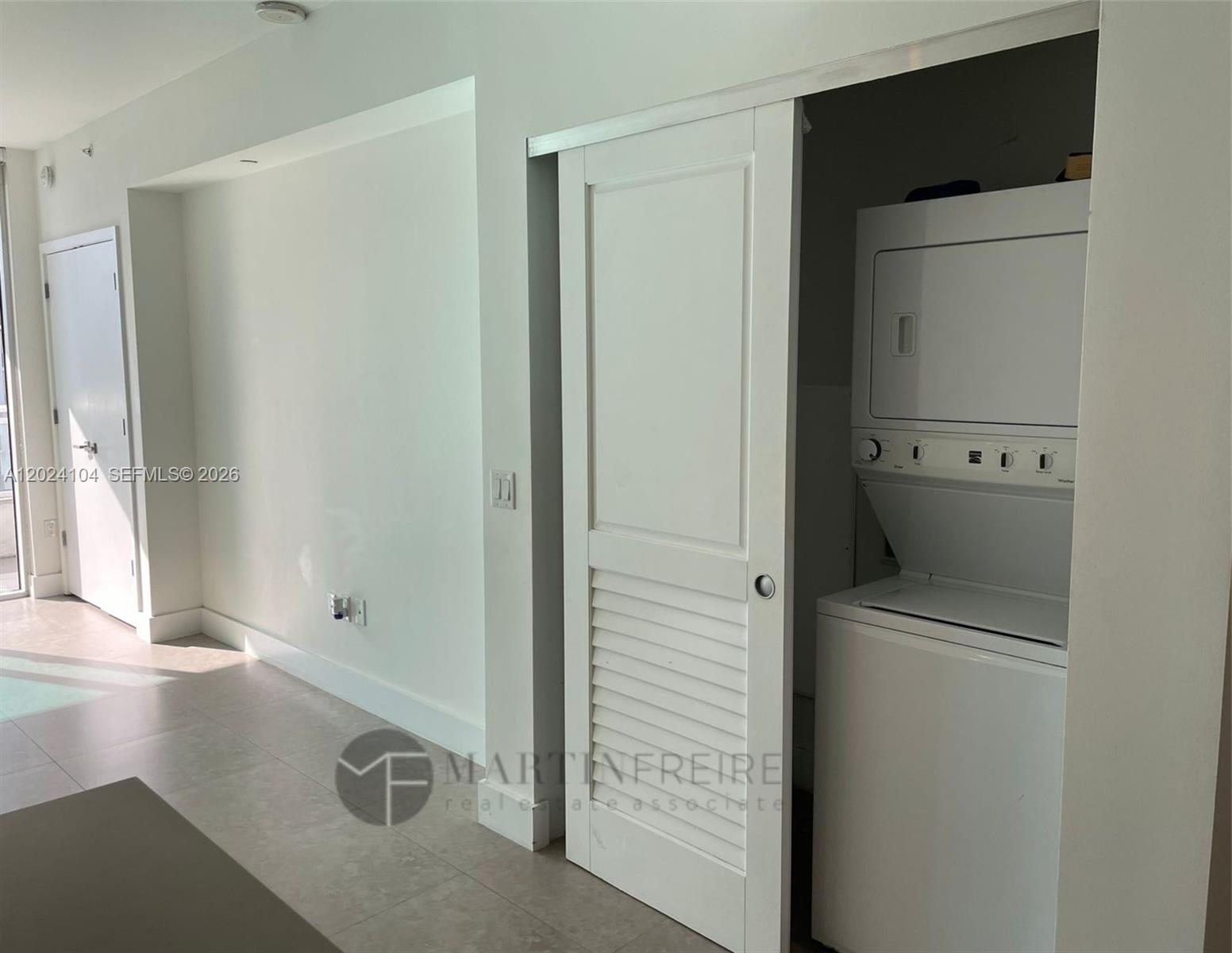 A white stacked washer and dryer unit is housed in a closet with a sliding door — 1080 Brickell Ave # 2005, Miami FL 33131, MIAMI, FL