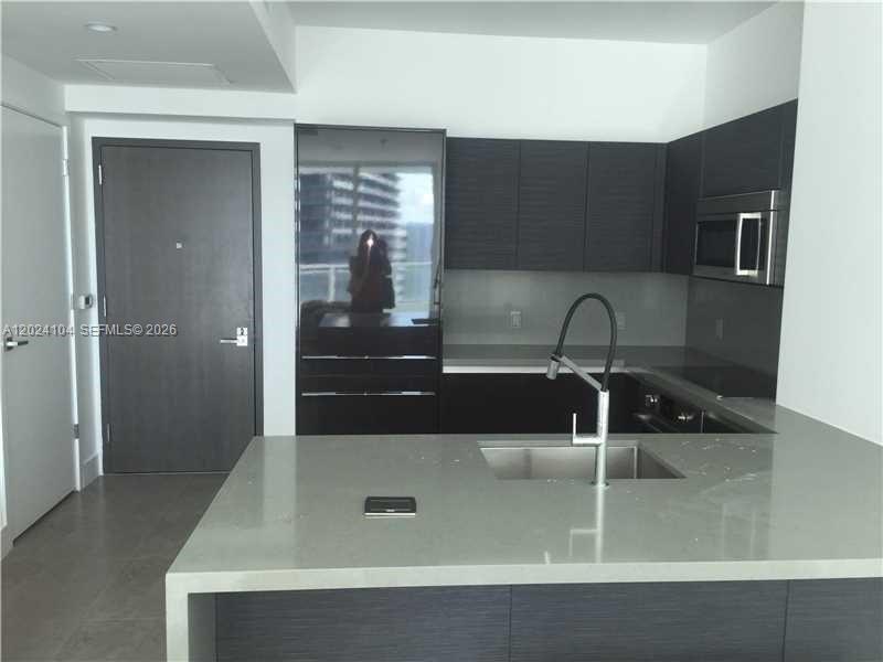 A modern kitchen features dark cabinetry, a gray quartz island, and a stainless steel sink — 1080 Brickell Ave # 2005, Miami FL 33131, MIAMI, FL