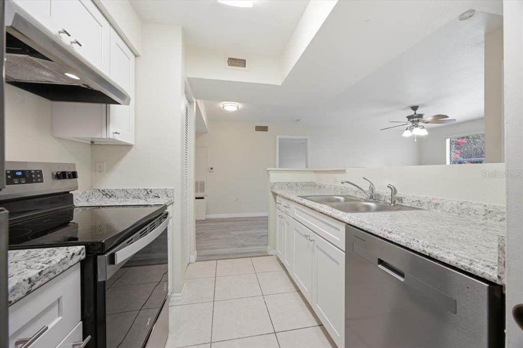 A kitchen with white cabinets, granite countertops, stainless steel appliances, and tile flooring — 3004 PARKWAY BOULEVARD UNIT 106, KISSIMMEE, FL