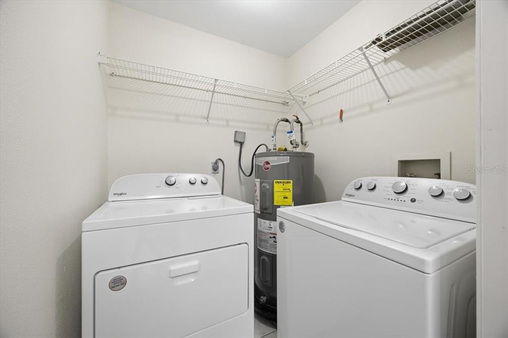 A laundry room features a white washer and dryer next to a water heater — 3004 PARKWAY BOULEVARD UNIT 106, KISSIMMEE, FL