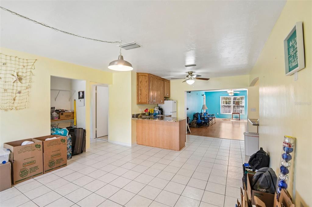 A kitchen with wooden cabinets and a breakfast bar opens into a tiled living area — 7446 PINEHURST DRIVE, SPRING HILL, FL