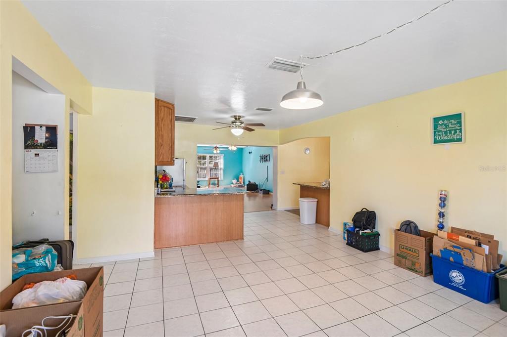 A living area with light yellow walls and white tile flooring leads to a kitchen — 7446 PINEHURST DRIVE, SPRING HILL, FL