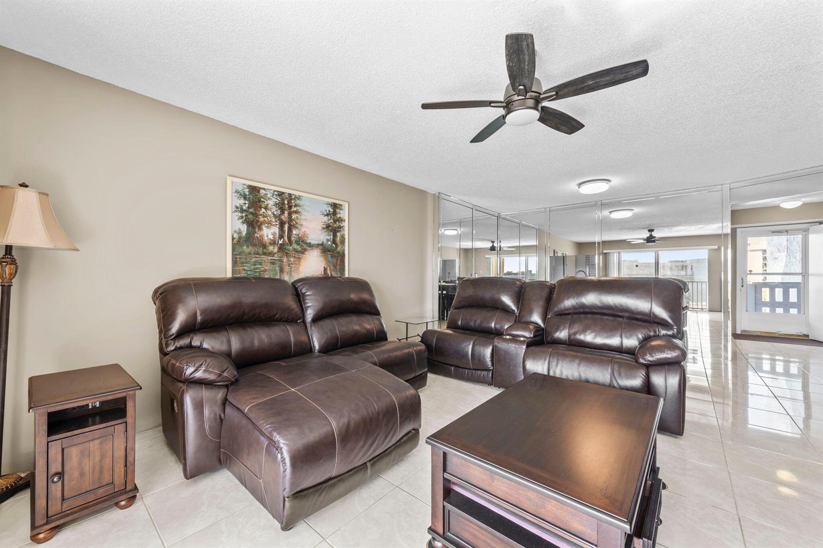 A living room features brown leather reclining sofas, a coffee table, and mirrored walls — 170 SE 5th Avenue Apt 505, Dania Beach FL 33004, DANIA BEACH, FL
