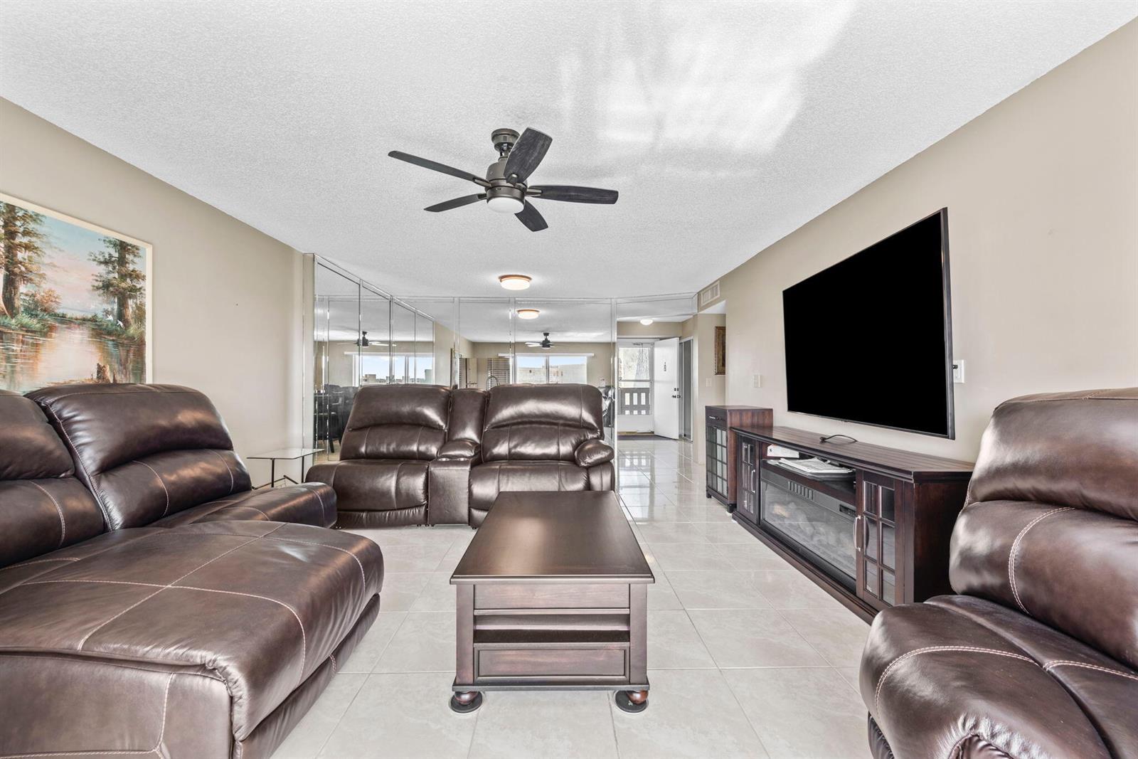 A living room features brown leather furniture, a coffee table, and a large wall-mounted television — 170 SE 5th Avenue Apt 505, Dania Beach FL 33004, DANIA BEACH, FL