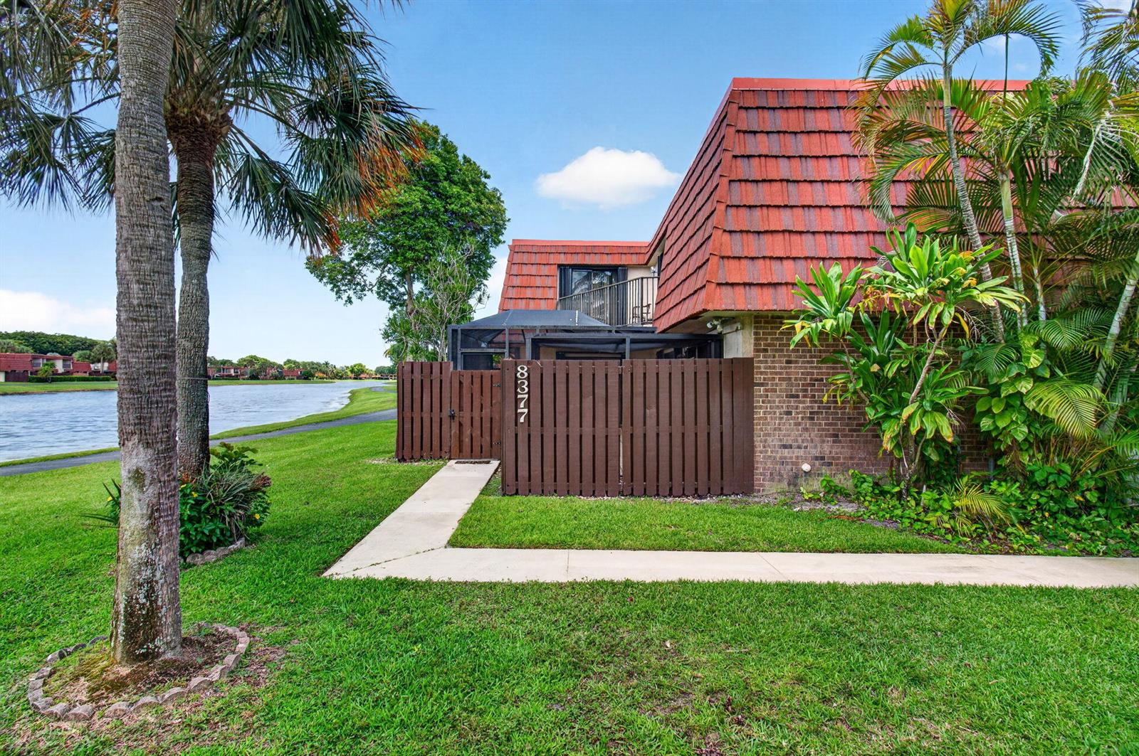 A brown wooden fence encloses a patio area next to a brick building with red shingles — 8377 Boca Rio Drive, Boca Raton FL 33433, BOCA RATON, FL