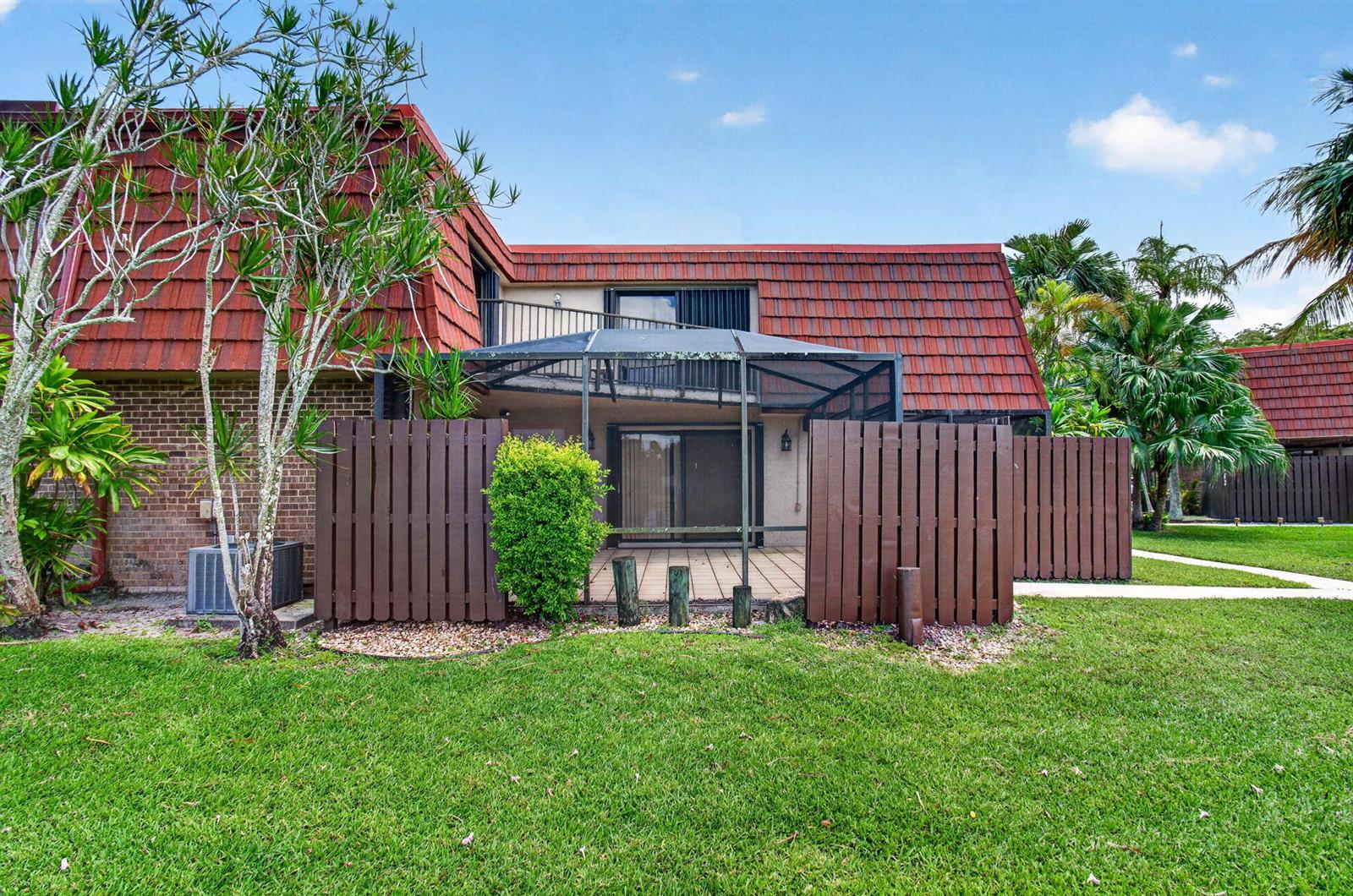 A two-story townhouse exterior with a screened-in patio, wooden privacy fence, and red tile roof — 8377 Boca Rio Drive, Boca Raton FL 33433, BOCA RATON, FL