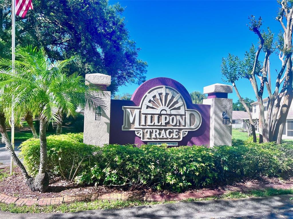 A sign for Millpond Trace stands in front of a landscaped area with trees — 7828 HARDWICK DRIVE UNIT 927, NEW PORT RICHEY, FL