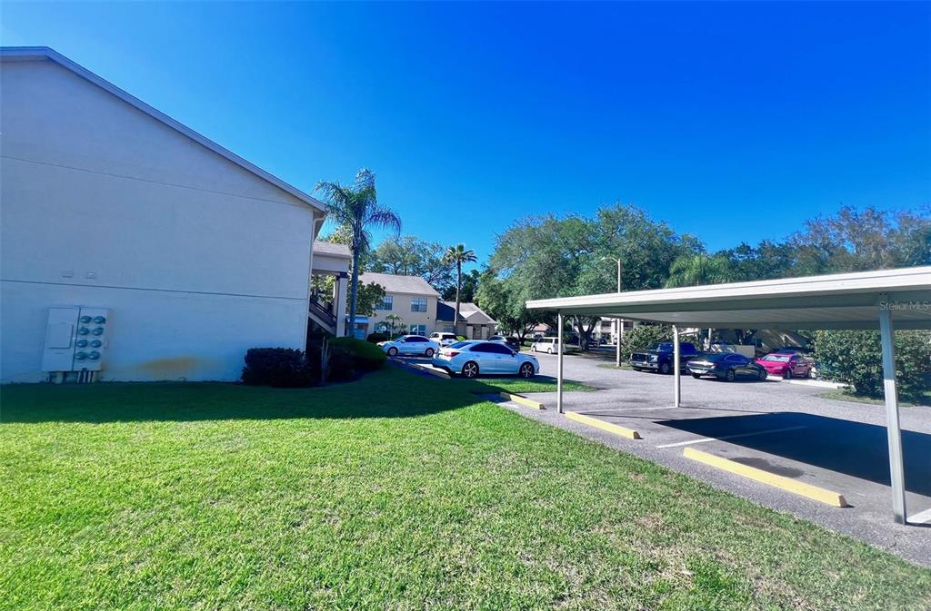 A grassy lawn sits beside a multi-story building and a covered parking structure — 7828 HARDWICK DRIVE UNIT 927, NEW PORT RICHEY, FL