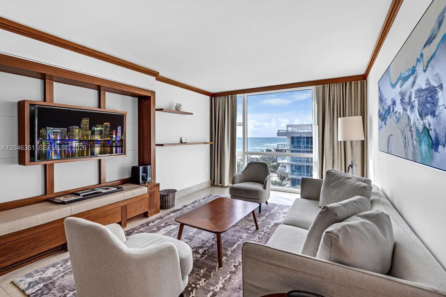 A living room features a wooden media wall, a sofa, armchairs, and an ocean view — 6801 Collins Ave, Miami Beach FL 33141, MIAMI BEACH, FL