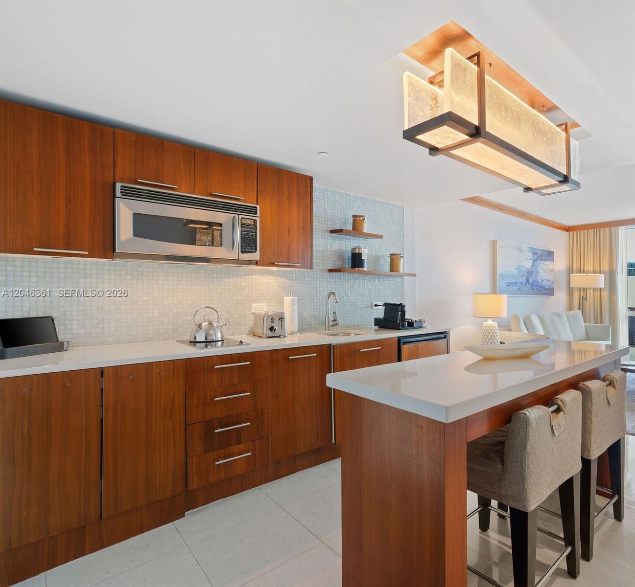 A modern kitchen features wood cabinets, white countertops, a breakfast bar, and a pendant light — 6801 Collins Ave, Miami Beach FL 33141, MIAMI BEACH, FL