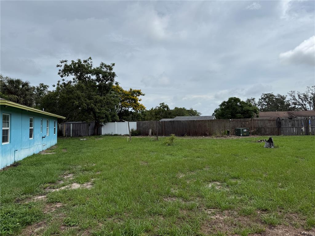 A grassy backyard features a blue house exterior, a wooden fence, and several trees — 6093 ASHLAND DRIVE, SPRING HILL, FL