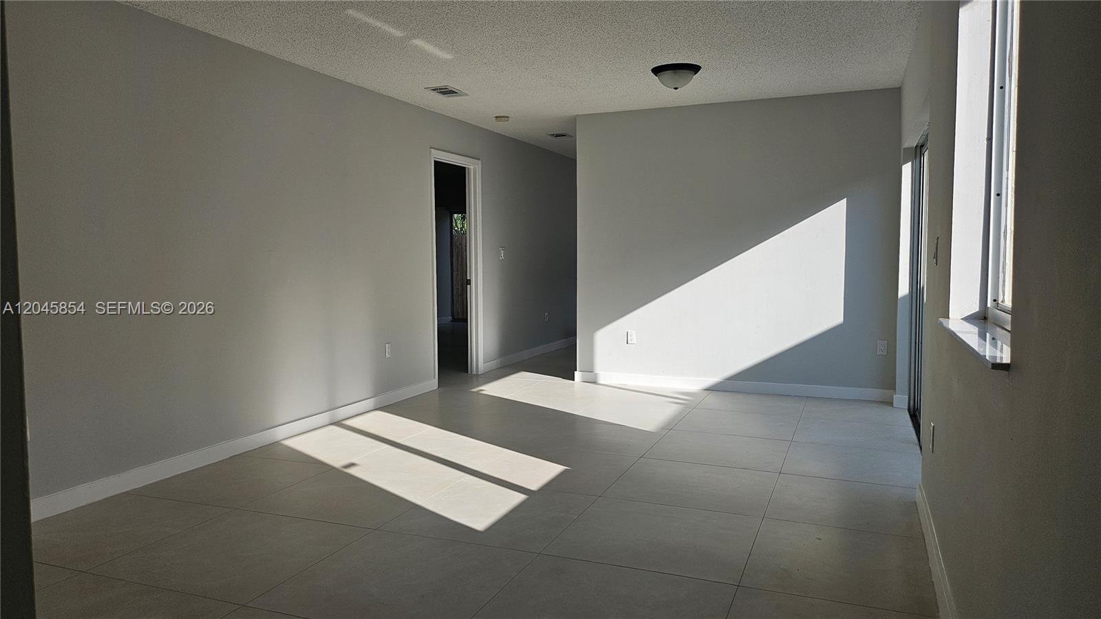An empty room features light gray walls, large beige floor tiles, and a sliding glass door — 16125 SW 137th Ct, Miami FL 33177, MIAMI, FL