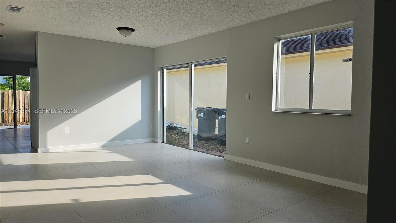 An empty room with light-colored tile flooring, a sliding glass door, and a single window — 16125 SW 137th Ct, Miami FL 33177, MIAMI, FL