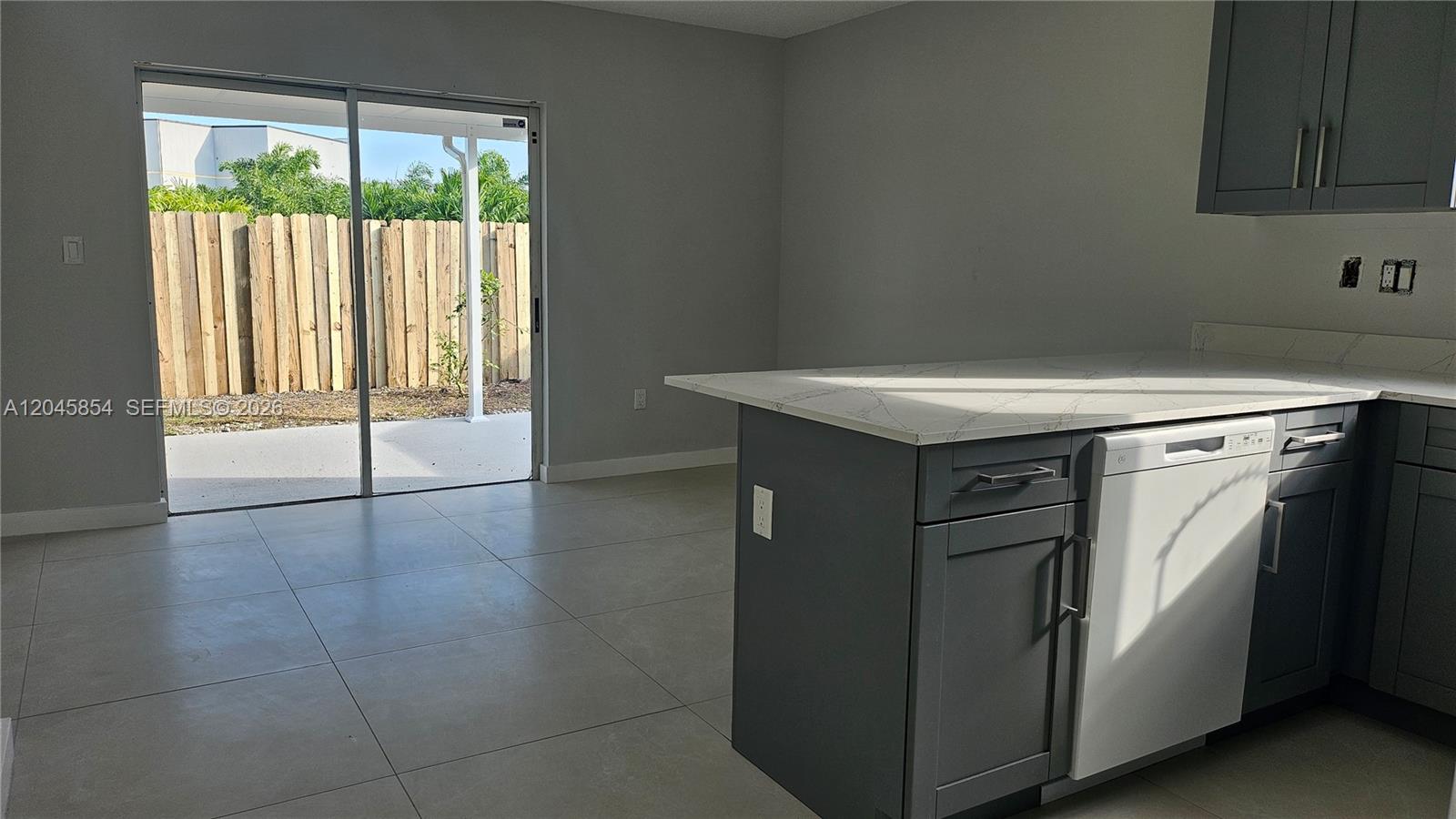 A kitchen with gray cabinets and a white dishwasher opens to a patio with fencing — 16125 SW 137th Ct, Miami FL 33177, MIAMI, FL
