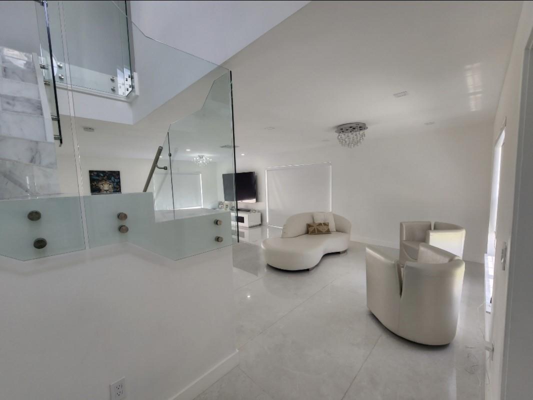 A modern living room features white tile floors, a curved sofa, and a glass staircase railing — 9706 NW 51st Terrace, Doral FL 33178, DORAL, FL