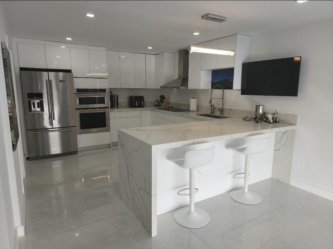 A modern kitchen features white glossy cabinets, stainless steel appliances, and a marble-patterned waterfall island — 9706 NW 51st Terrace, Doral FL 33178, DORAL, FL