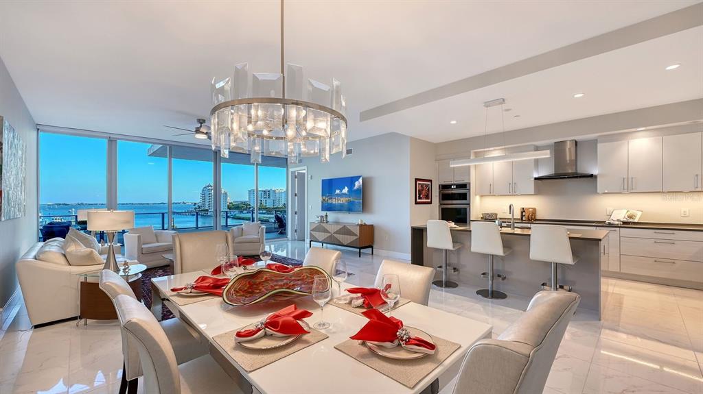 A modern open-concept living and dining area features a kitchen island, chandelier, and waterfront views — 1155 N GULFSTREAM AVENUE UNIT 401, SARASOTA, FL