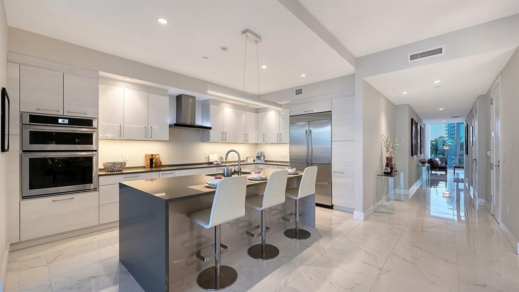 A modern kitchen features light wood cabinetry, a dark island with bar seating, and tile flooring — 1155 N GULFSTREAM AVENUE UNIT 401, SARASOTA, FL