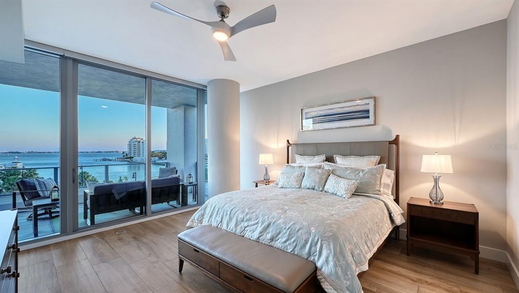 A bedroom features a king bed, wood-look tile flooring, and floor-to-ceiling windows overlooking the water — 1155 N GULFSTREAM AVENUE UNIT 401, SARASOTA, FL