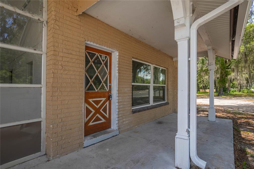 A covered porch with a brick wall, a wooden door, and white support columns — 8929 E GULF TO LAKE HIGHWAY, INVERNESS, FL