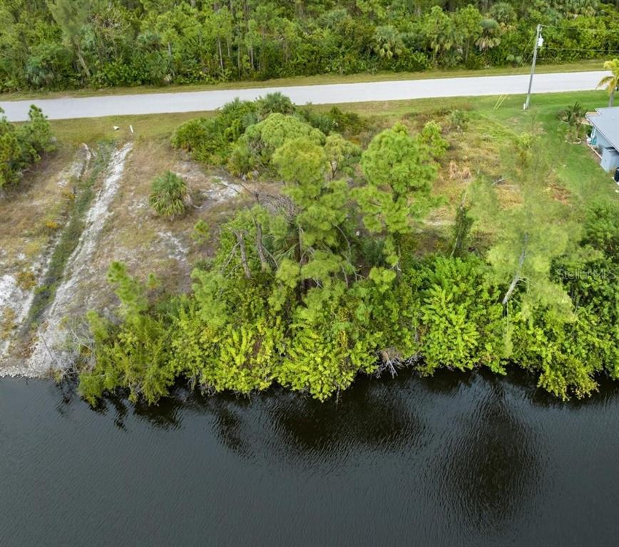 An aerial view shows a vacant, wooded waterfront lot adjacent to a paved road — 15664 ALDAMA CIRCLE, PORT CHARLOTTE, FL