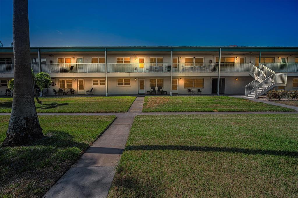 A two-story apartment building with exterior walkways, a staircase, and a grassy lawn at dusk — 5216 81ST STREET N UNIT 5, ST PETERSBURG, FL