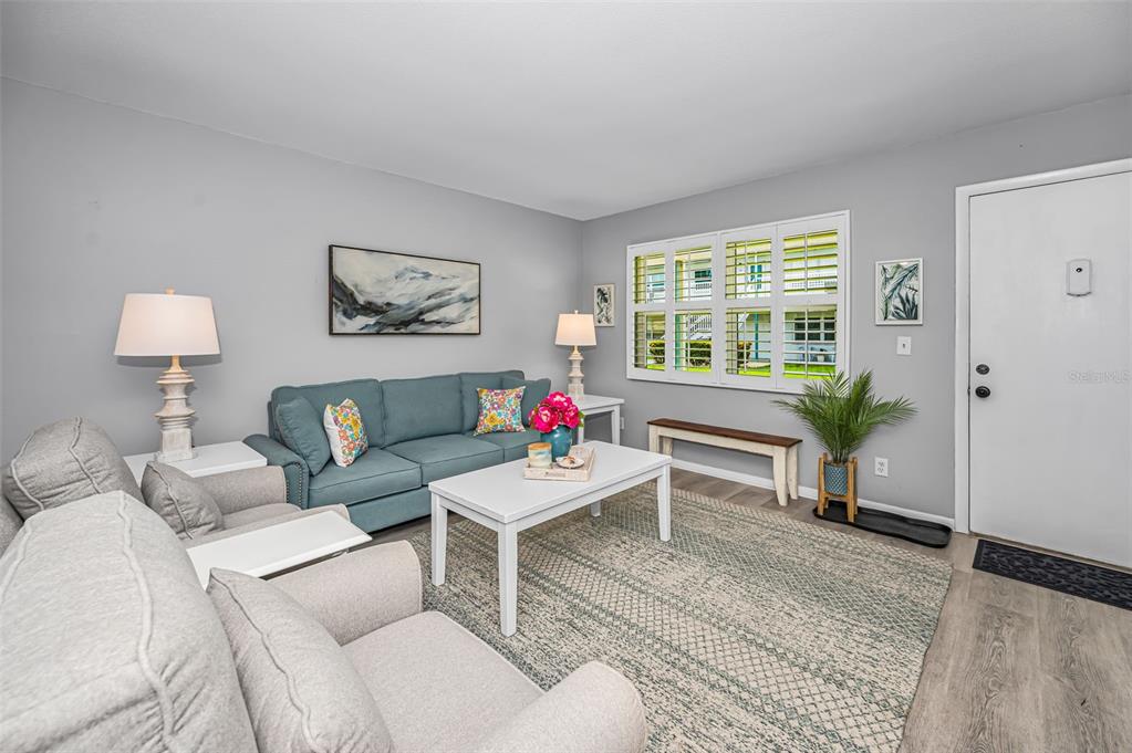 A living room features a blue sofa, gray armchairs, a white coffee table, and shutters — 5216 81ST STREET N UNIT 5, ST PETERSBURG, FL