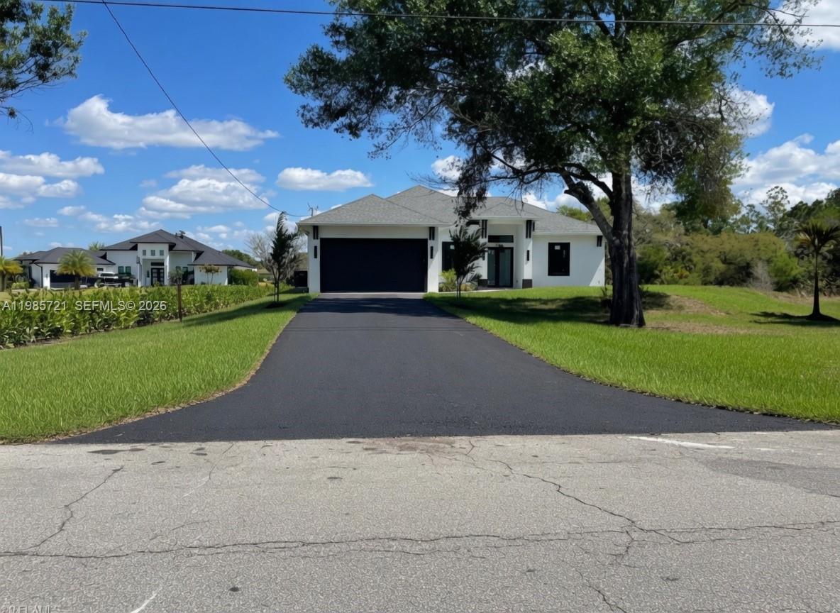 A modern single-story house with a black garage door and asphalt driveway under a blue sky — 6186 N Everglades blvd, Naples FL 34120, NAPLES, FL