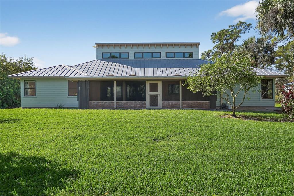 The exterior of a light green house with a metal roof and a screened-in porch — 8535 SE MAY TERRACE, HOBE SOUND, FL