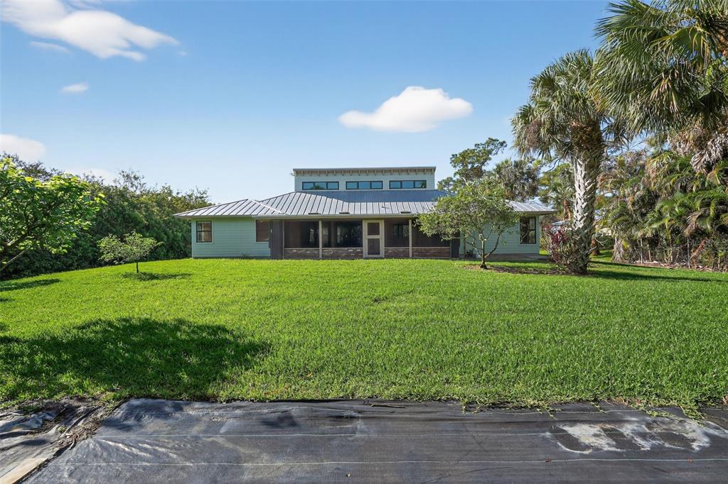 A light green house with a metal roof and a screened porch faces a lawn — 8535 SE MAY TERRACE, HOBE SOUND, FL