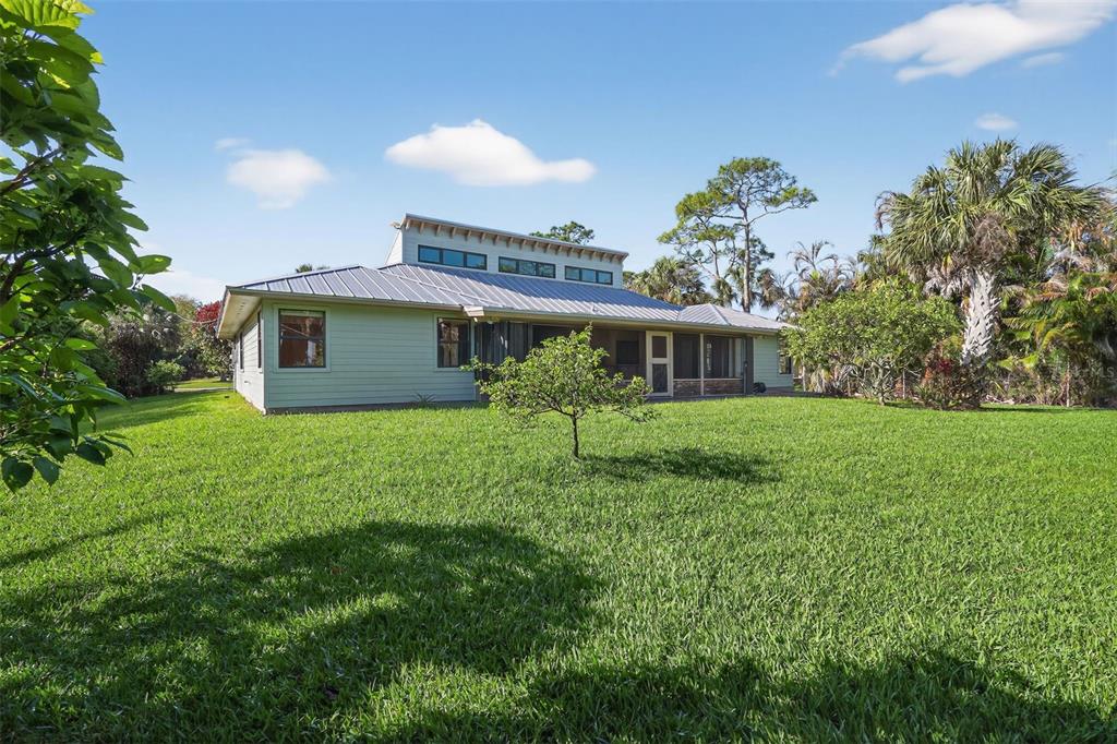 A light green house with a metal roof and a large backyard under a blue sky — 8535 SE MAY TERRACE, HOBE SOUND, FL
