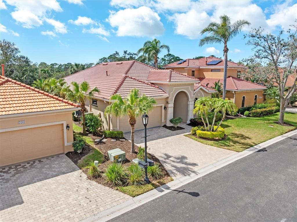 An exterior view of a tan house with a tiled roof and a paved driveway — 5142 COTE DU RHONE WAY, SARASOTA, FL
