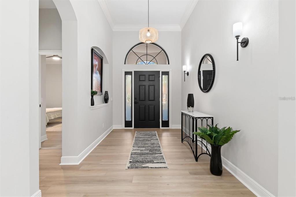 A bright entryway features light wood floors, a black front door, and a console table — 5142 COTE DU RHONE WAY, SARASOTA, FL