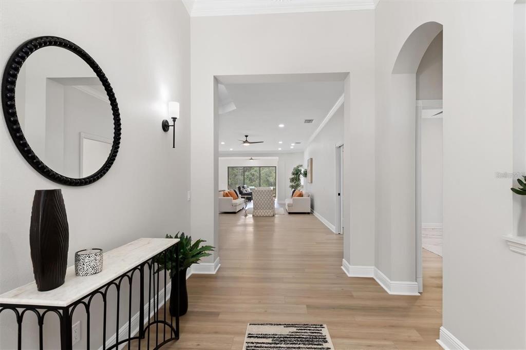 A bright foyer with light wood floors leads into a living room with white walls — 5142 COTE DU RHONE WAY, SARASOTA, FL