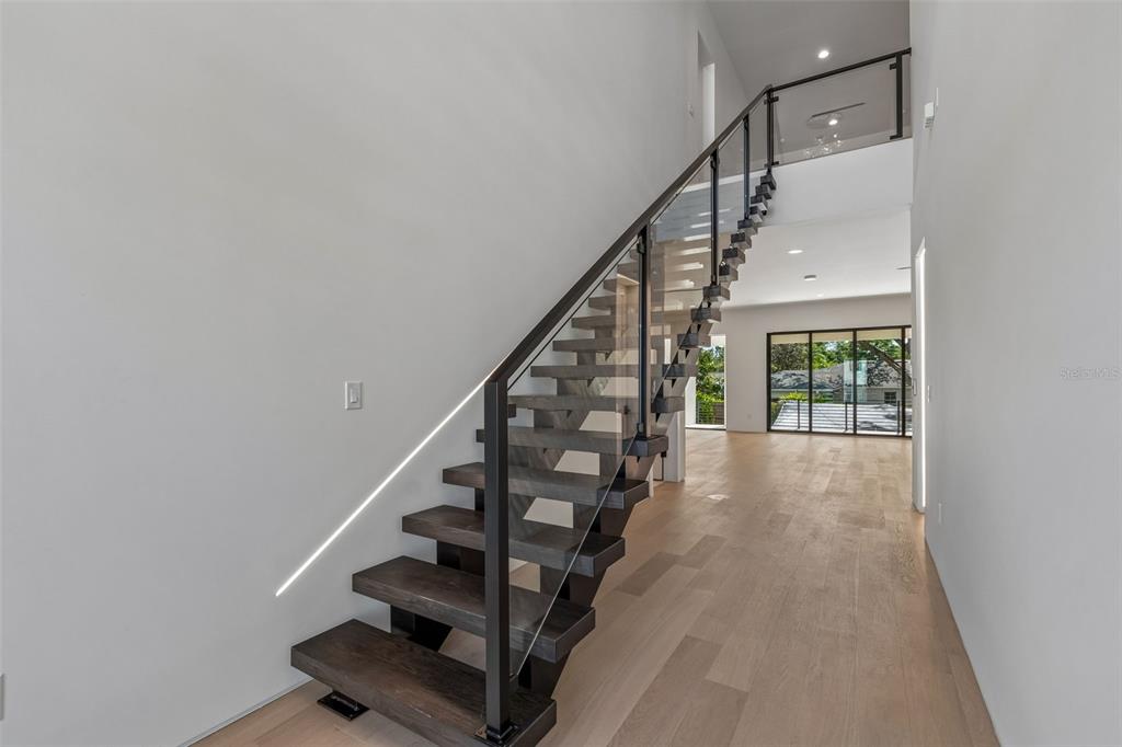 A modern staircase with dark wood treads and a glass railing stands in a bright hallway — 206 S TREASURE DRIVE, TAMPA, FL