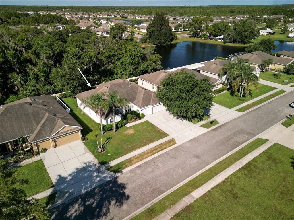 An aerial view shows a suburban house with a brown roof and a backyard pond — 695 GRAPE IVY LANE, NEW SMYRNA BEACH, FL
