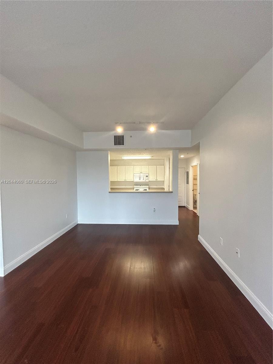 An empty living area with dark wood floors leads to an open kitchen pass-through — 1155 Main St # 301, Jupiter FL 33458, JUPITER, FL