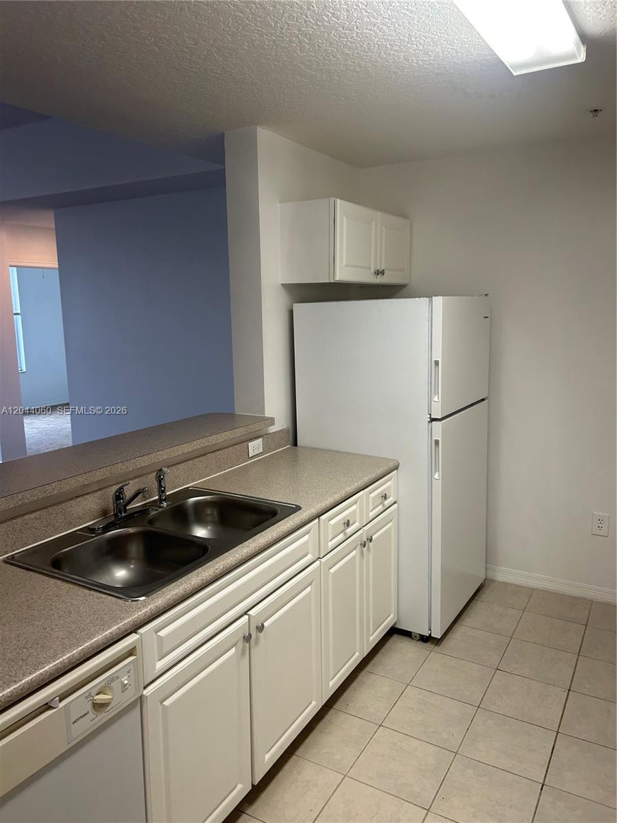 A kitchen features white cabinets, a double sink, a white refrigerator, and tiled flooring — 1155 Main St # 301, Jupiter FL 33458, JUPITER, FL