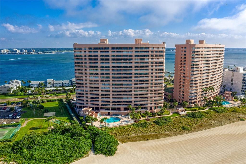 An aerial view shows two tall, tan residential buildings situated on a sandy beach — 1310 GULF BOULEVARD UNIT 10B, CLEARWATER BEACH, FL