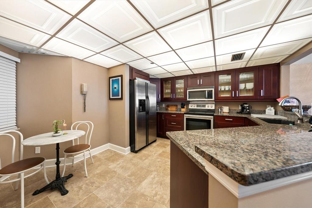 A kitchen features dark wood cabinets, granite countertops, stainless steel appliances, and a drop ceiling — 1310 GULF BOULEVARD UNIT 10B, CLEARWATER BEACH, FL