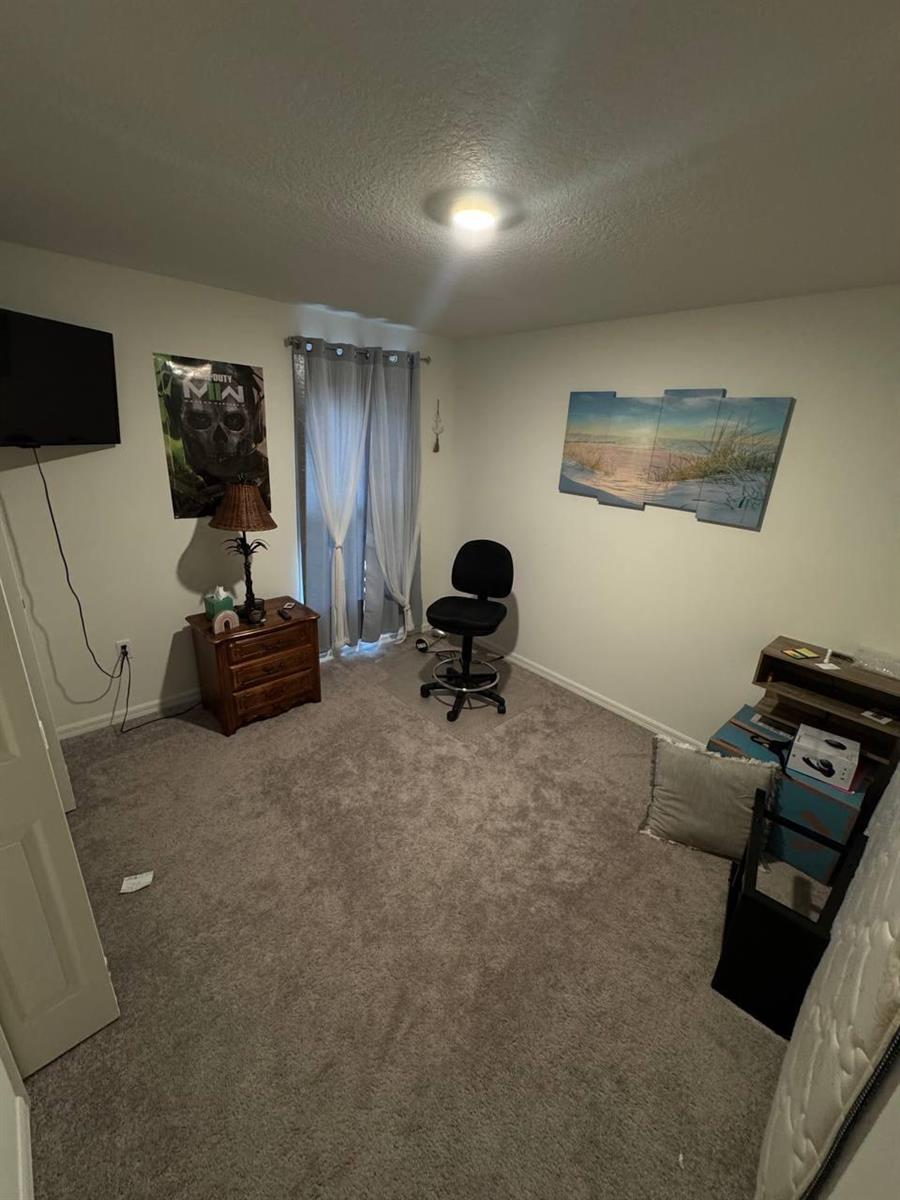 A bedroom with gray carpet, a window with curtains, a nightstand, and wall art — PORT ST. LUCIE, FL