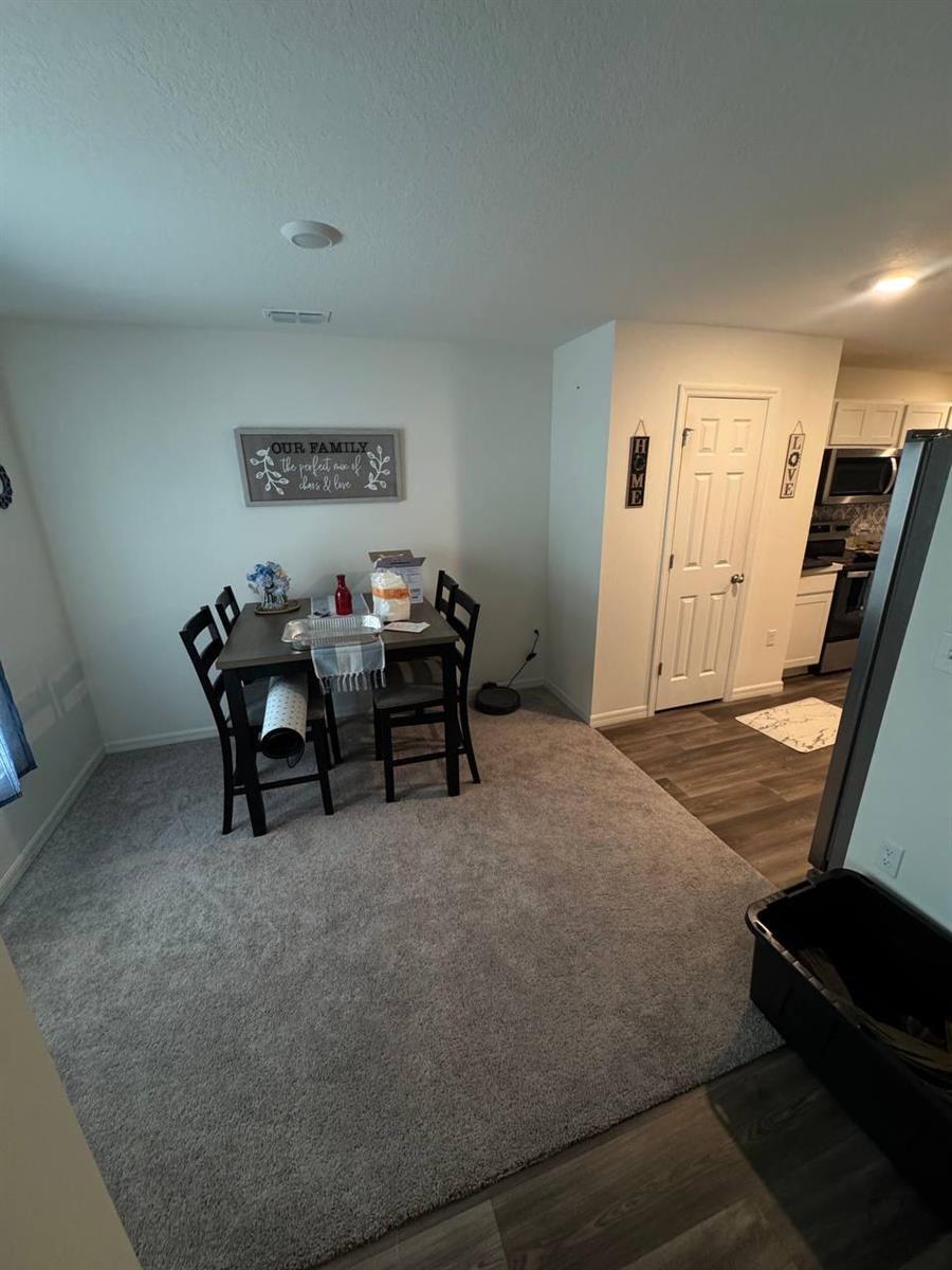 A dining area with a table and four chairs sits on carpet next to a kitchen — PORT ST. LUCIE, FL