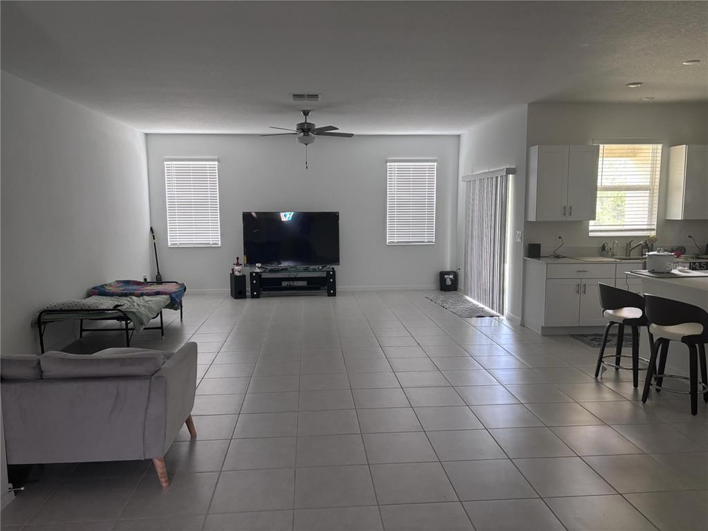 An open-concept living room features white tile flooring, a ceiling fan, and an adjacent kitchen — 17747 TAWNY MALT PLACE, LAND O LAKES, FL