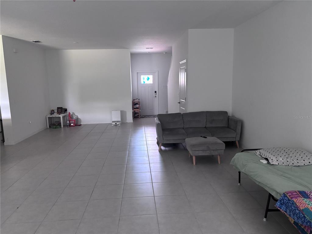 A living room with light tile flooring, a gray sofa, and a front entry door — 17747 TAWNY MALT PLACE, LAND O LAKES, FL