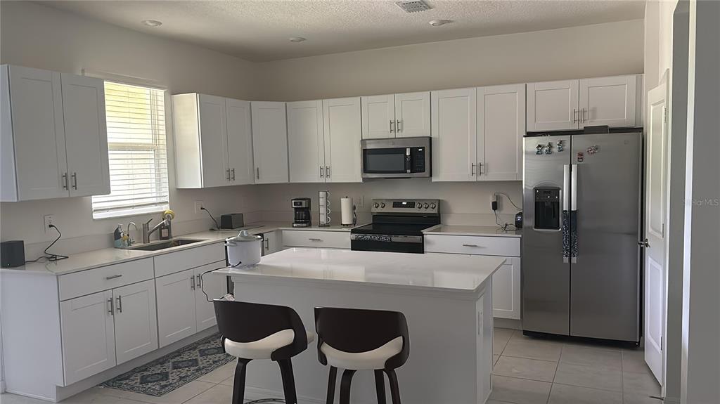 A kitchen features white cabinets, stainless steel appliances, a center island, and tile flooring — 17747 TAWNY MALT PLACE, LAND O LAKES, FL